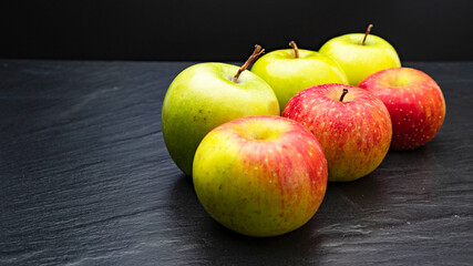 Three ripe fresh green apples and tree red apples on black table and dark background. Free copy space. School snacks or organic food concept