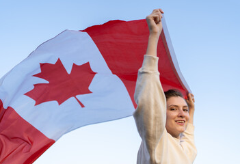 A woman carries the Canadian flag in her hands, it waving in the wind. Immigrant in a free country with a national symbol