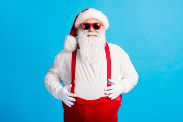 Fototapeta na wymiar Photo of modern trendy fat santa claus touch hands big stomach x-mas christmas north-pole creature wear headwear cap suspenders overalls sunglass isolated blue color background