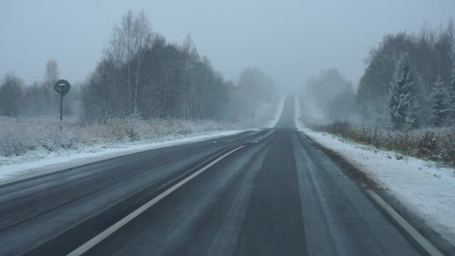 The car drives on a winter road during a snowfall. View through the windshield