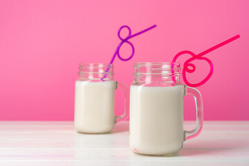 Glass jars with flavoured milkshakes against pink background