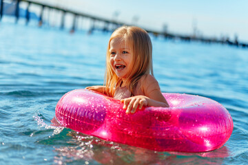 Little girl with pink inflatable circle bathing in sea
