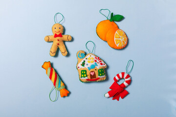Flat lay Handmade felt Christmas ornaments: sweets, gingerbread house, gingerbread man, orange and its slice. are on the blue background. Consept of hand sewing, cute Christmas heroes.