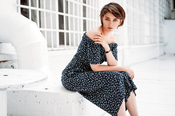 Young beautiful brunette girl with short hair wear long dress and sitting outdoor in white scenery