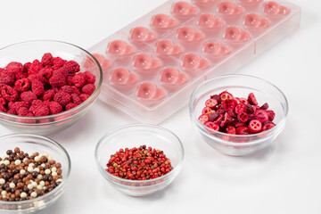 Heart shape confectionery mold with melted ruby chocolate and natural dried berries species filling on white worktop, hand-crafted premium homemade candies. Chocolate production, candymaking concept