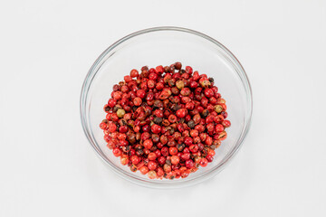Red milled pepper corns balls in glass bowl isolated on white background, organic hot species, dried red peppercorns, natural spice. Food concept, chili pepper cosmetic ingredients. Text space