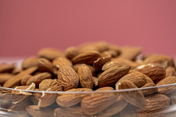 Closeup raw peeled almonds in glass bowl on pink background, organic fresh nuts, natural delicious snack, cooking baking ingredients. Nuts texture macro. Healthy vegetarian food concept, text space