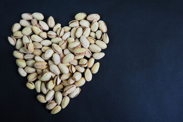 many pistachio seeds are laid out in the form of a heart on a black background top view . grain kind of pistachio