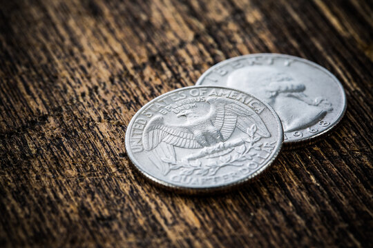 Detailed close-up of many shiny american quarter coins on grungy wooden background. Selective focus, shallow depth of field.