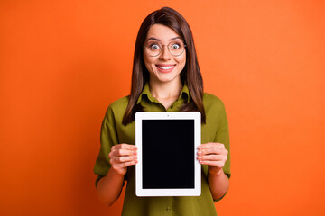 Photo portrait of amazed female student showing screen empty space on tablet staring in eyewear isolated on vivid orange color background