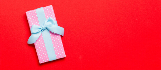 wrapped Christmas or other holiday handmade present in paper with blue ribbon on red background. Present box, decoration of gift on colored table, top view with copy space
