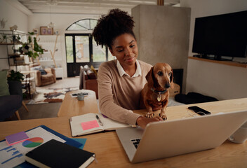 Happy african woman working at home using laptop during quarantine sitting with dog