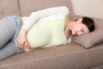 Beautiful pregnant woman suffering belly ache lying on a sofa at home