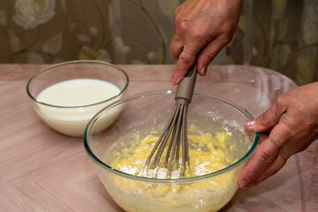 Women's hands knead the dough with different ingredients-milk, flour, butter, sugar and egg for homemade pancakes.