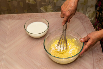 Women's hands knead the dough with different ingredients-milk, flour, butter, sugar and egg for homemade pancakes.