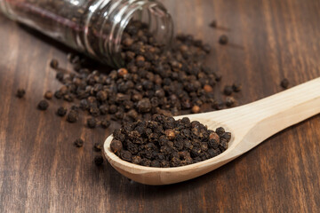 Piper nigrum - black peppercorns; photo on dark wooden background.