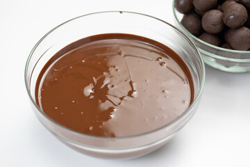 Closeup dark or milk melted chocolate in glass bowl isolated on white background. Organic couverture high-quality chocolate, hand-crafted homemade candies. Truffles, confectionery, dessert concept