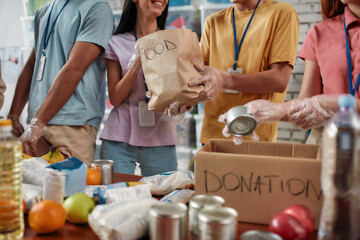 Cropped shot of male and female volunteers holding paper bag with food while packing donation for...
