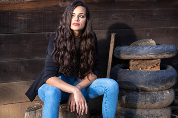 Beautiful brunette girl in jeans, sitting next to a pile of old tires