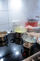 Woman cooking on cooker in the kitchen with hot steam and pots on a ceran stove to cook delicious meals for the family as healthy nutrition and a yummy lunch and dinner preparation
