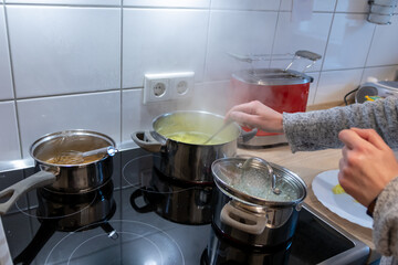 Woman cooking on cooker in the kitchen with hot steam and pots on a ceran stove to cook delicious meals for the family as healthy nutrition and a yummy lunch and dinner preparation