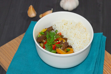 Roast beef with sweet pepper and white rice. White plate, garlic in the background, dark background.