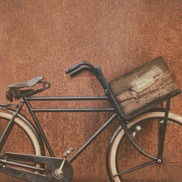 Black cargo bicycle with old wooden transport crate and leather saddle in front of a corten steel wall