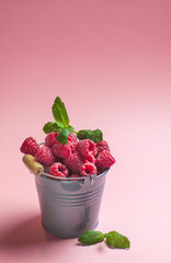 ripe raspberries in a grey bucket on pink background served as healthy seasonal dessert