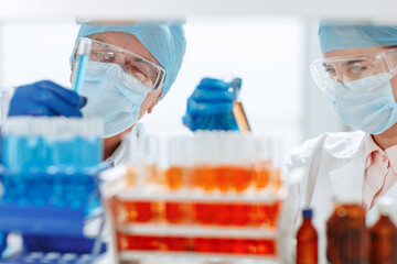 scientists in protective masks standing in front of a rack of test tubes .