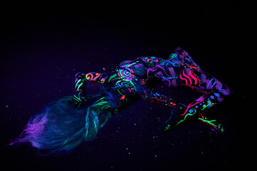 Art woman body art on the body dancing in ultraviolet light. Bright abstract drawings on the woman body neon color. Colored hair and face