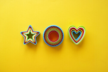 Plastic molds of multi colors for making cookies in the shape of a openwork circle, stars and hearts on a yellow background.