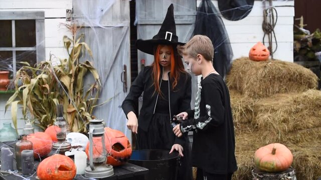 children a boy in a skeleton costume and a girl in a witch costume at a Halloween party brew a potion