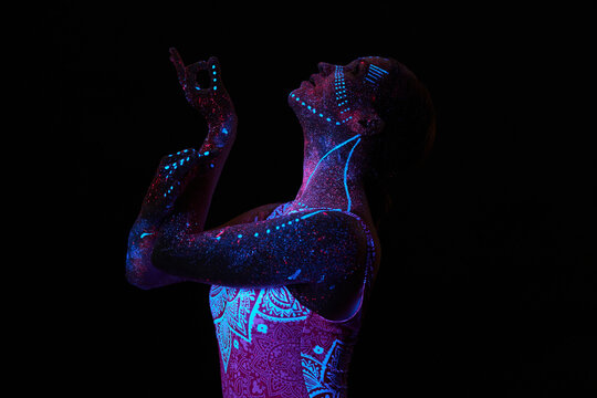 Art woman cosmos in ultraviolet light. Entire body is covered with colored droplets. Girl posing in the dark. Noise, out of focus