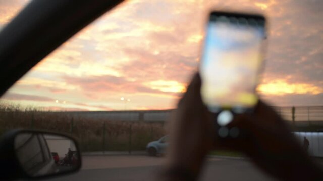 Making Photo with Mobile Smart Phone of a Pink Sunset Sky from a Car