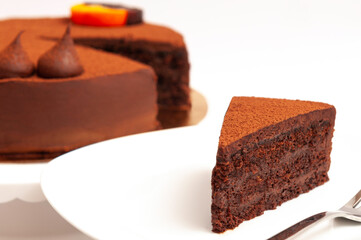 White plate with a piece of delicious chocolate cake and the cake in background