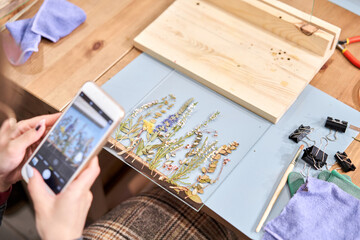 A woman takes a photo for a blog and social network. Master class on creating frame with Herbarium...