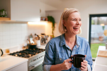 Laughing Mature Woman At Home In Kitchen Drinking Coffee