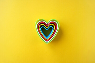 Plastic molds of multi colors for making cookies in the shape of a hearts on a yellow background.