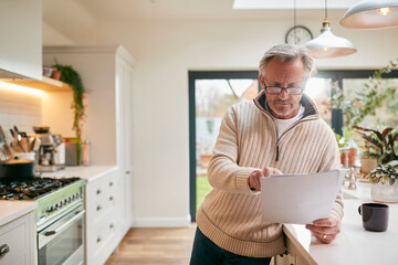 Mature Man At Home In Kitchen Drinking Coffee And Looking At Financial Documents