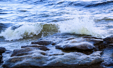 waves run onto the shore and crash against the rocks, creating many splashes and splashes near the shore. river surf in stormy weather near a stone pebble coast with foamy splashing waves.