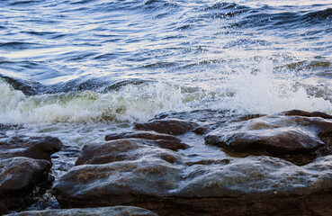 waves run onto the shore and crash against the rocks, creating many splashes and splashes near the shore. river surf in stormy weather near a stone pebble coast with foamy splashing waves.