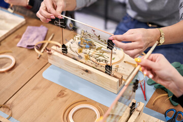 A woman glues metal tape for soldering with a soldering iron. Master class on creating frame with...