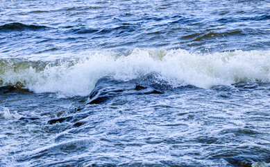 Naklejka premium waves run onto the shore and crash against the rocks, creating many splashes and splashes near the shore. river surf in stormy weather near a stone pebble coast with foamy splashing waves.