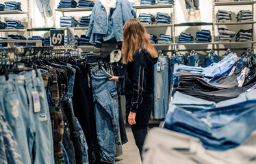 Smiling girl shopper choosing new jeans at store