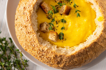 Pumpkin puree soup in a plate of bread close up, pumpkin soup with thyme , cheese and croutons on a white wooden background, top view