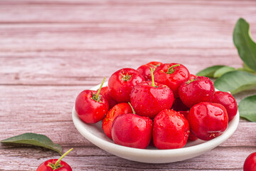 Ripe red cherries in a ceramic dish with leaves on a wooden table. Space for text. Sweet organic berries. Concept of healthy fruits