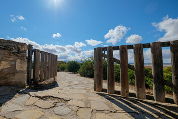 Puerta de madera que muestra el camino de piedra hacia los arboles , bajo el cielo azul con nubes blancas
