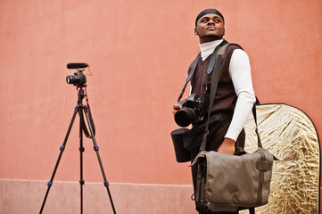 Young professional african american videographer holding professional camera with pro equipment. Afro cameraman wearing black duraq making a videos.