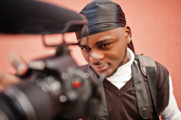 Young professional african american videographer holding professional camera with pro equipment. Afro cameraman wearing black duraq making a videos.