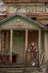 Portrait of a smiling young woman with curly hair on the porch of an old wooden house. Outside.